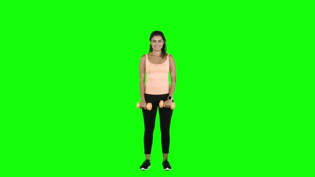 Full length of young woman exercising with two dumbbells while standing in the studio. Shot in 4k resolution with green screen background