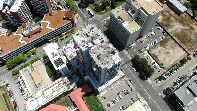 Sweeping spiral Aerial shot of a busy construction site in Perth CBD with workers and a crane operator working hard on a high-rise building with traffic buzzing below in East Perth, Western Australia.