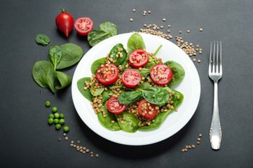 Salad of baby spinach leaves, green lentils, cherry tomatoes, olive oil and lemon juice in a bowl on a dark surface. A dietary dish. Vegetarian, vegan concept