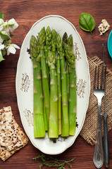 Boiled asparagus in a white oval plate on a brown wooden board. Extra diet low-calorie seasonal...