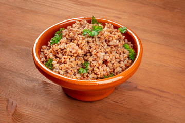 Cooked buckwheat in a rustic earthenware bowl, garnished with fresh parsley, on a dark wooden background with a place for text