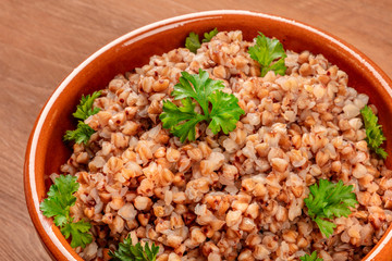 A closeup photo of boiled buckwheat in a rustic earthenware bowl, garnished with fresh parsley