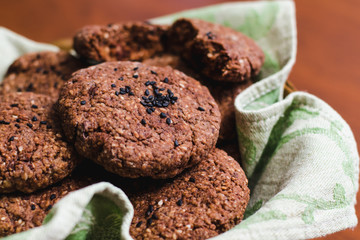 Homemade chocolate oatmeal cookies with white and black sesame seeds on a brown wooden table close up
