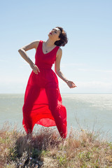 Brunette woman in red dress dancing in nature in summer