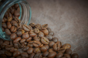roasted coffee beans poured from a glass jar. angular placement of the coffee object. on dark...