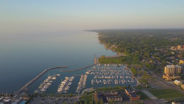 AERIAL: initially perpendicular wide portrait view of the shoreline of Kenosha then tilts down and closes in on a boat moving through the harbor.