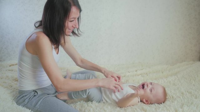 Mother massaging little son in bed at home. Strengthening exercises for babies, home healthcare concept.
