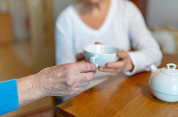 Rentnerin bekommt von der Pflegekraft eine Tasse Tee gereicht