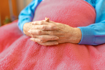 Rentnerin hält die Hände gefaltet und mit einer Decke zugedeckt