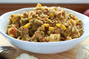 Close up view of cauliflower rice with vegetables. Organic vegan cauliflower rice with peas, carrot, corn and onion on wooden table. Horizontal view.