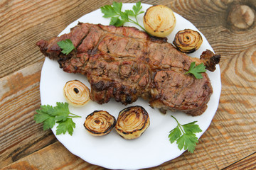 Grilled pork meat with onion and parsley on wooden table