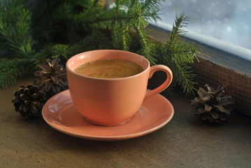 Hot coffee in a pink ceramic cup, fir branches and winter snowy window. Christmas or New Year card.