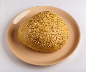 Bun with sesame seeds on a plate on a white background.