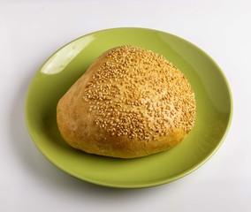 Bun with sesame seeds on a plate on a white background.
