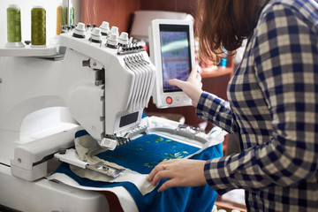 Close-up of woman working on modern computerized specially engineered embroidery machine with...