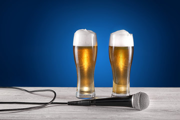 Two glass beer and microphone on white wooden desk. Blue background. Free space for text