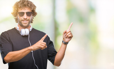 Handsome hispanic man listening to music wearing headphones over isolated background smiling and looking at the camera pointing with two hands and fingers to the side.