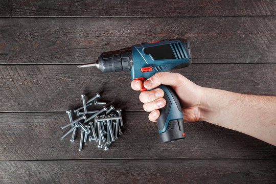 Blue electric screwdriver in male hand black wooden table with  bolts. Top view