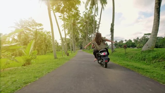 Happy couple tripping by motorcycle on tropical road at sunset time. Outdoor shot of young couple riding motorbike. Man riding on a motorcycle with girlfriend on rural road.