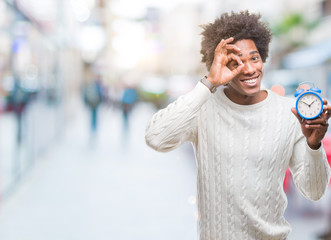 Afro american man holding vintage alarm clock over isolated background with happy face smiling doing ok sign with hand on eye looking through fingers