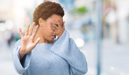 Young beautiful african american woman wearing a sweater over isolated background covering eyes with hands and doing stop gesture with sad and fear expression. Embarrassed and negative concept.