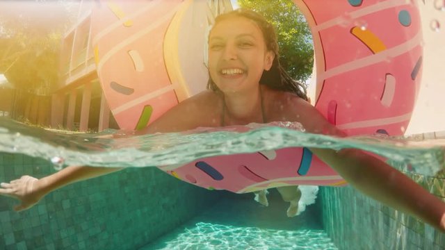 Woman with sunglasses in blue bikini lying in inflatable pink donut float in pool on sunny summer day. Look at camera. Woman bikini swimming pool on watermelon rubber ring relaxing vacation