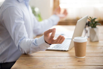 Close up of peaceful male employee sit at office desk meditating at workplace, calm man worker...