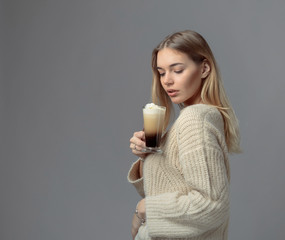 Beautiful blonde in a sweater holding a mug of coffee with cream.