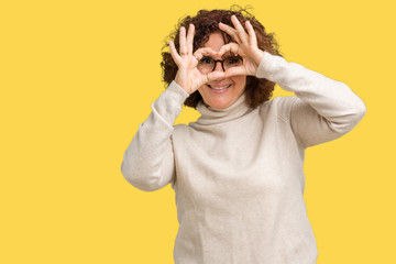 Beautiful middle ager senior woman wearing turtleneck sweater and glasses over isolated background Doing heart shape with hand and fingers smiling looking through sign