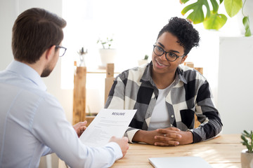 Male employer holding resume talking with African American female job candidate at interview, black...