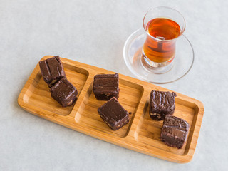 Chocolate cake cut into squares and served on a board with Turkish tea in a tea glass.
