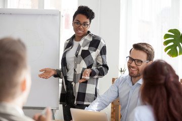 Millennial African American mentor or coach interacting with office employees during flipchart...