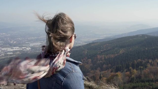 Young woman on a top of amountain looking at the landscape in strong wind, slow motion.