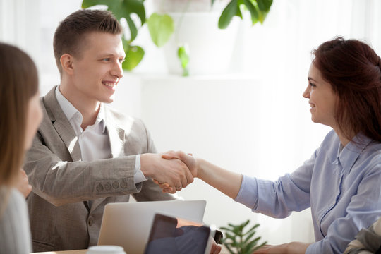 Smiling businessman shake hand of young female colleague getting acquainted at workplace, diverse employees handshake introducing at meeting, smiling man greeting coworker woman at briefing
