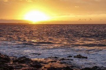 Dramatic sky at sunset over the sea. Orange landscape with rocks in foreground. Atlantic ocean seen from Lanzarote, Canary Islands, Spain.
