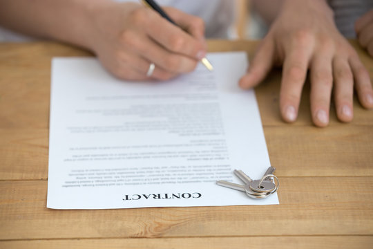 Close up of husband sign contract buying house from realtor or broker, man put signature on document, keys on table, taking mortgage or loan, renter finalize formal procedure closing deal with agent