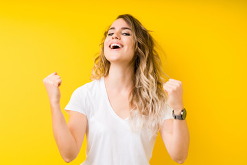 Young beautiful blonde woman over yellow background very happy and excited doing winner gesture with arms raised, smiling and screaming for success. Celebration concept.