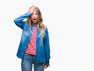 Beautiful young blonde woman over isolated background surprised with hand on head for mistake,...