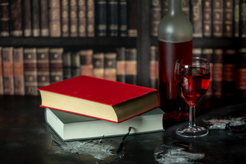 in a room full of books, on the table stands a glass and a bottle of red wine, next to them lies two books