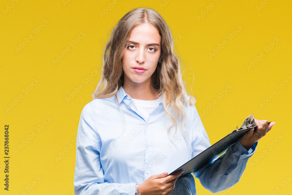 Wall mural Beautiful young blonde business woman holding clipboard over isolated background with a confident expression on smart face thinking serious