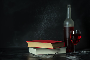 a glass and a bottle of red wine next to books on a black background