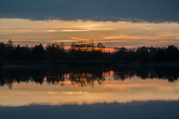 Trees on the shore of the lake and reflection of clouds after sunset