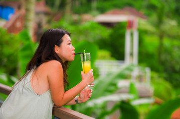 young beautiful and happy Asian Korean woman enjoying at holidays resort in tropical rice terrace smiling delighted drinking healthy orange juice