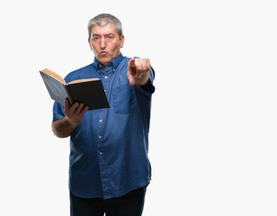 Handsome senior teacher man reading a book over isolated background pointing with finger to the camera and to you, hand sign, positive and confident gesture from the front