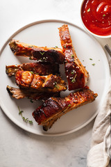 Bbq pork ribs with chili sauce on white plate. Pork ribs on slate background. Copy space.