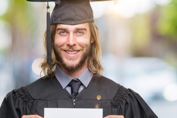 Young handsome graduate man with long hair holding blank paper over isolated background with a...