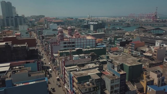 Aerial drone above capital city Colombo, Sri Lanka with the famous Red Mosque (Jami Ul-Alfar Mosque) in the distance with ocean, tall buildings, and a large cargo ship terminal/ container port dock