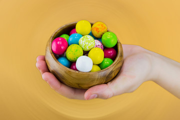 colorful multicolored dragee candy round green pink yellow in wooden bowl in hand gift for the spring holiday