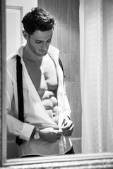Handsome man with muscular body unbuttoning shirt to reveal sixpack abs reflection in bathroom...