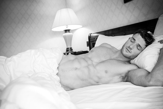 Handsome hunky muscular man with six pack abs sleeping in between white sheets in hotel bed